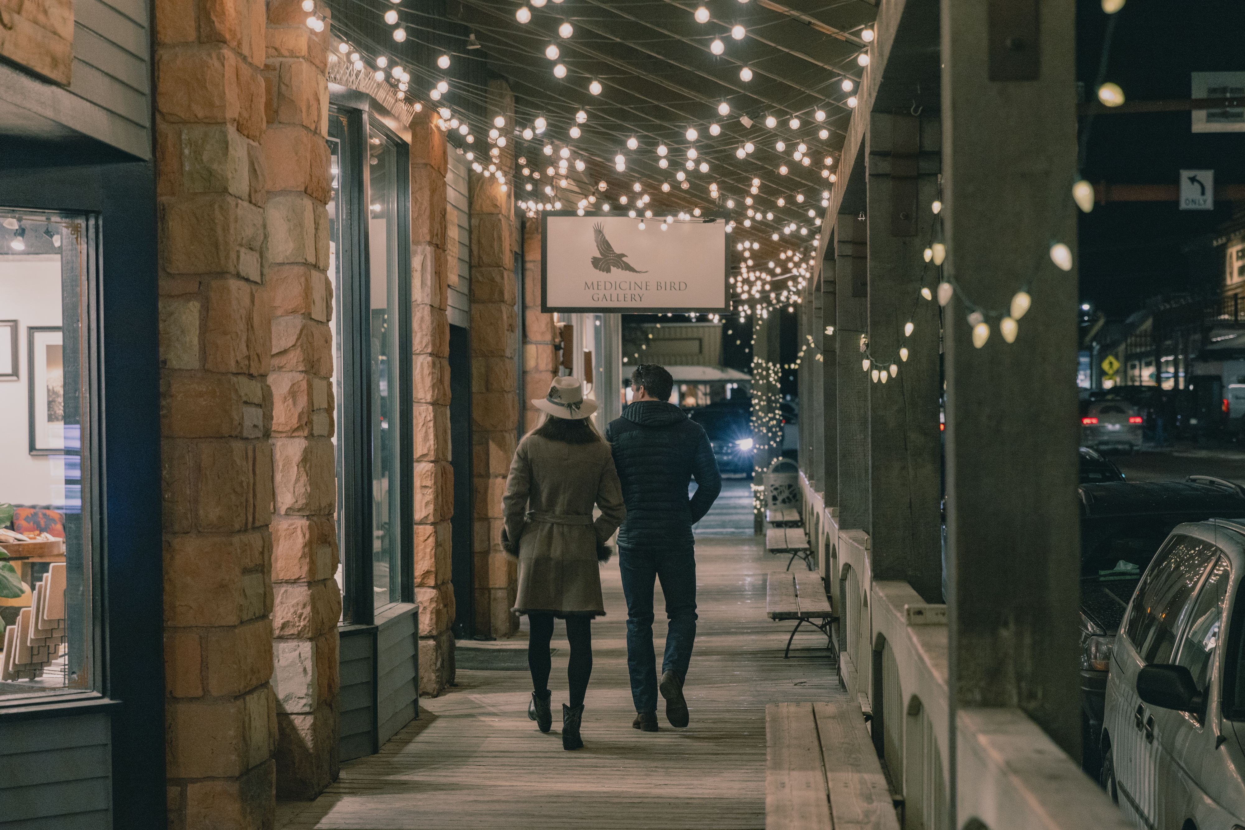 A couple walking arm in arm beneath string lights on a downtown Jackson boardwalk at night