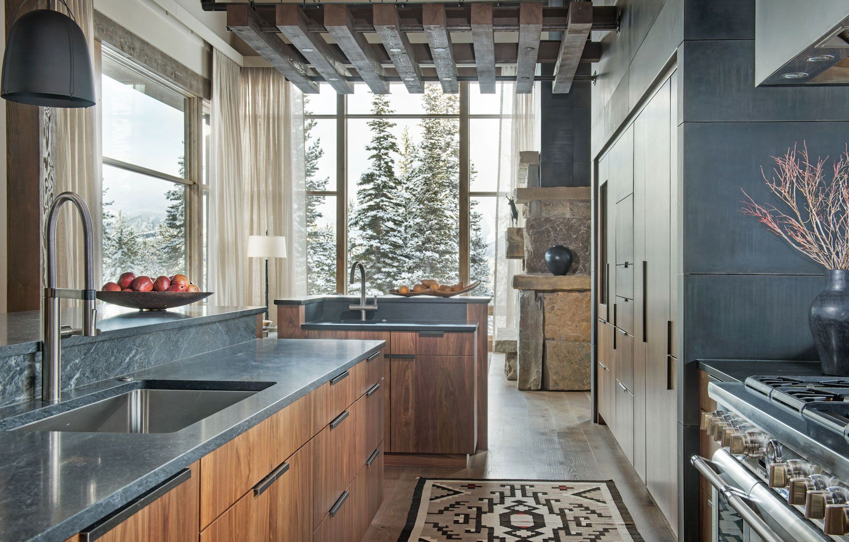 A luxury kitchen in walnut and dark stone, with windows overlooking a snowy forest