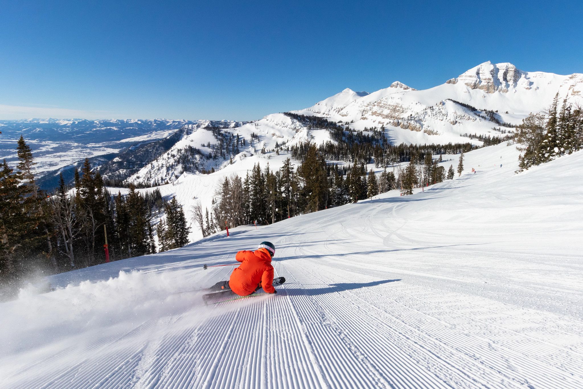 A skier carving fresh corduroy on a sunlit run high above the valley